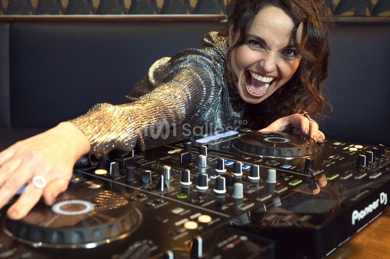 Femme souriante portant une tenue brillante, utilisant une table de mixage dans un environnement intérieur.