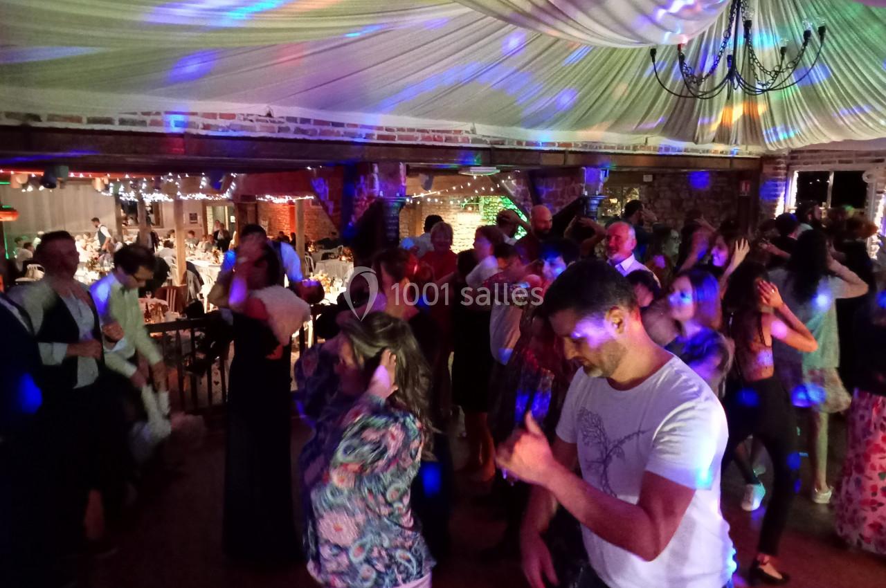 Groupe de personnes dansant sous des lumières colorées dans une salle décorée avec un plafond drapé et des guirlandes…