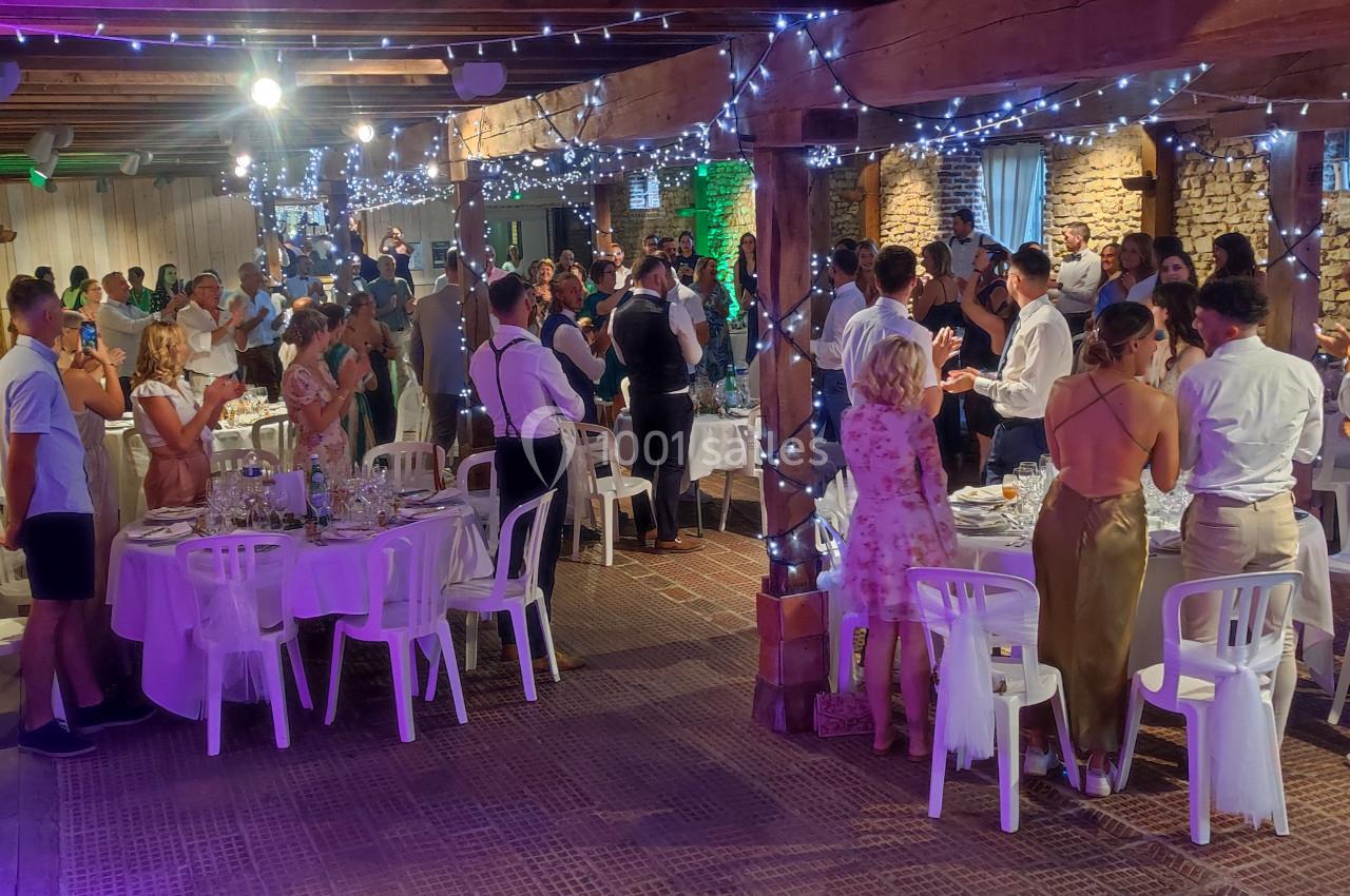 Salle de réception avec des invités debout et assis, décorée de guirlandes lumineuses et murs en pierre apparente.