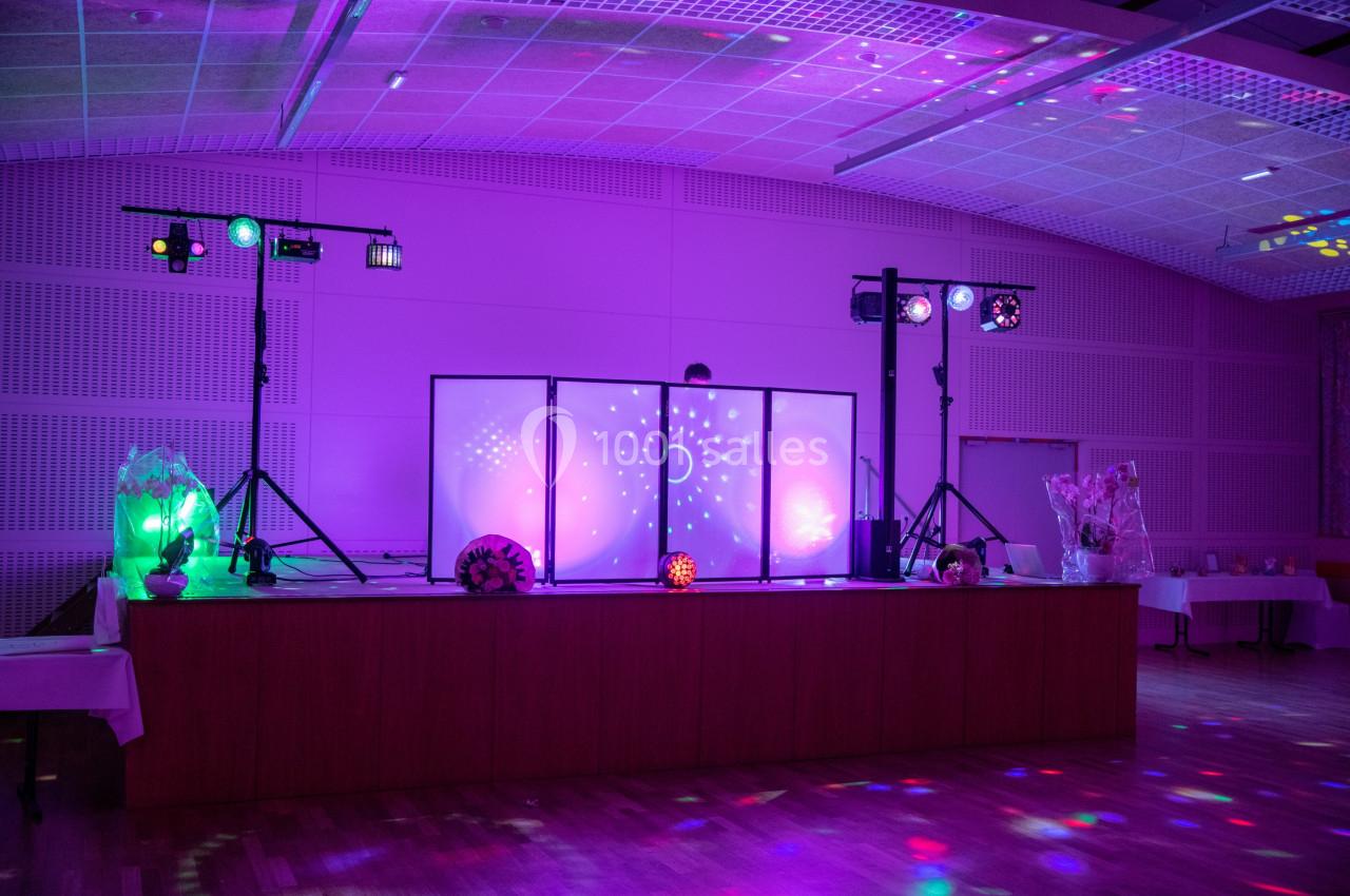 Scène de fête éclairée par des lumières colorées avec une table en bois et des équipements de sonorisation.