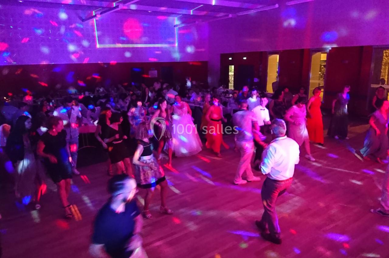 Des personnes dansent dans une salle éclairée par des lumières colorées lors d'une fête ou d'un événement.