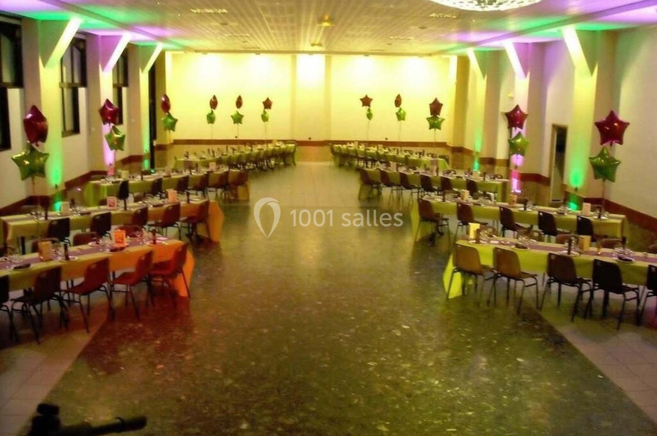 Salle de réception décorée avec des tables alignées, nappes colorées et ballons étoilés suspendus.