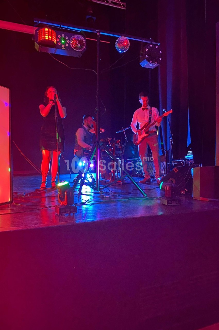 Un groupe de musiciens joue sur une scène éclairée par des lumières colorées dans une ambiance sombre.