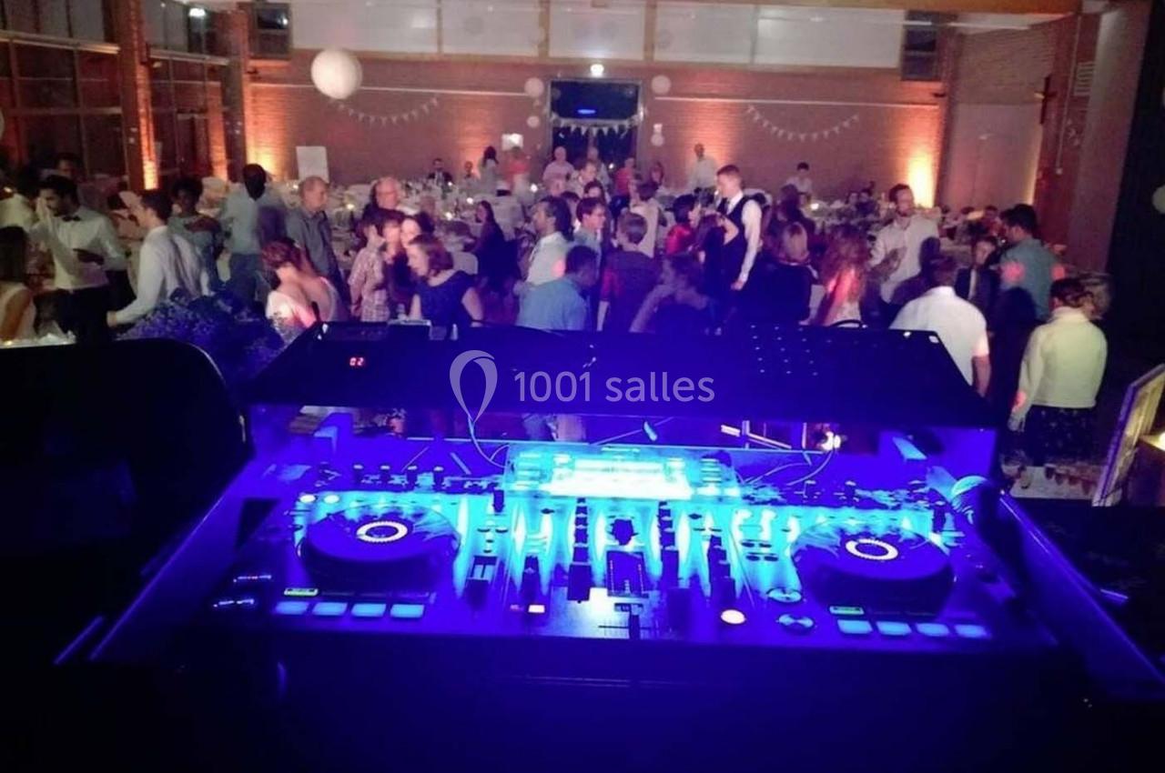 Vue depuis une table de mixage éclairée en bleu, avec des invités dansant et discutant dans une salle festive.