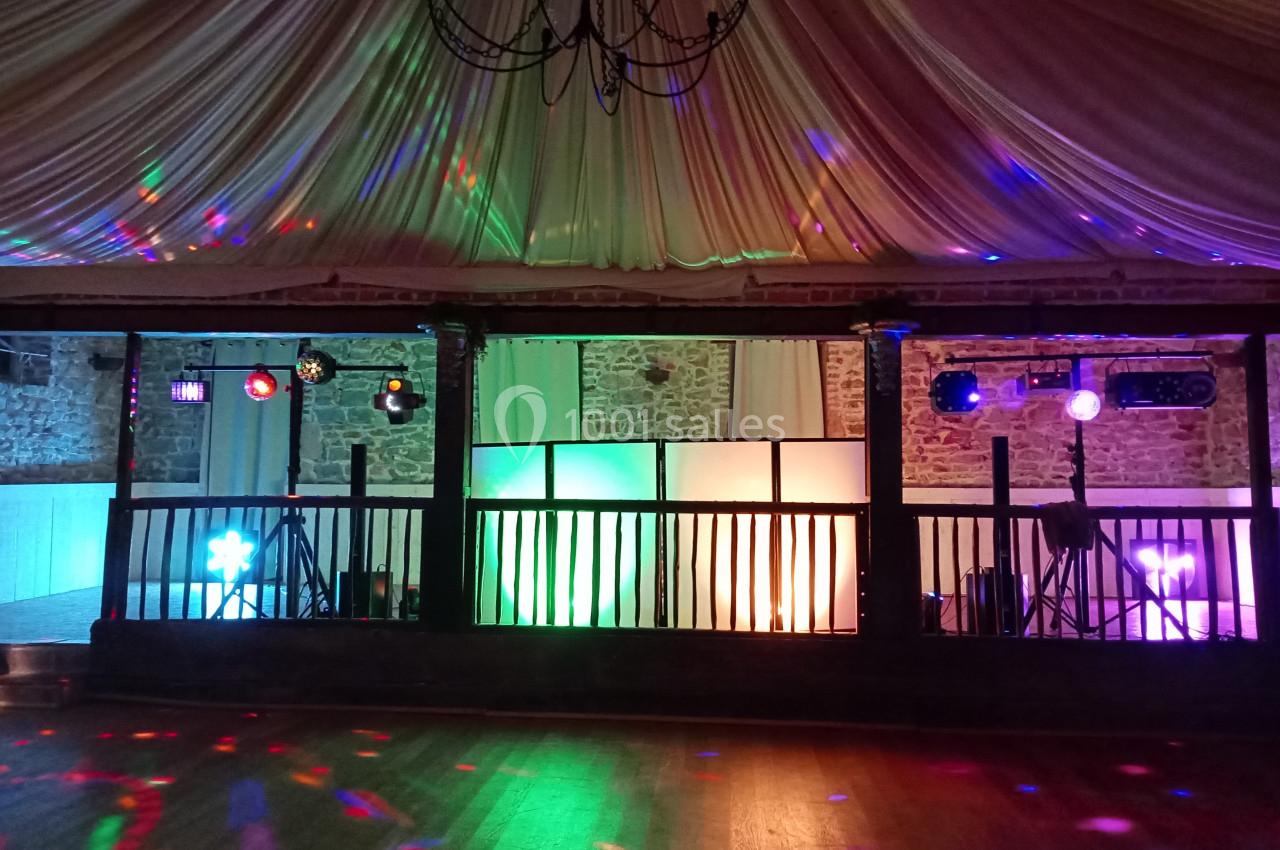 Salle de réception décorée avec un plafond drapé, des lumières colorées et une piste de danse en bois.
