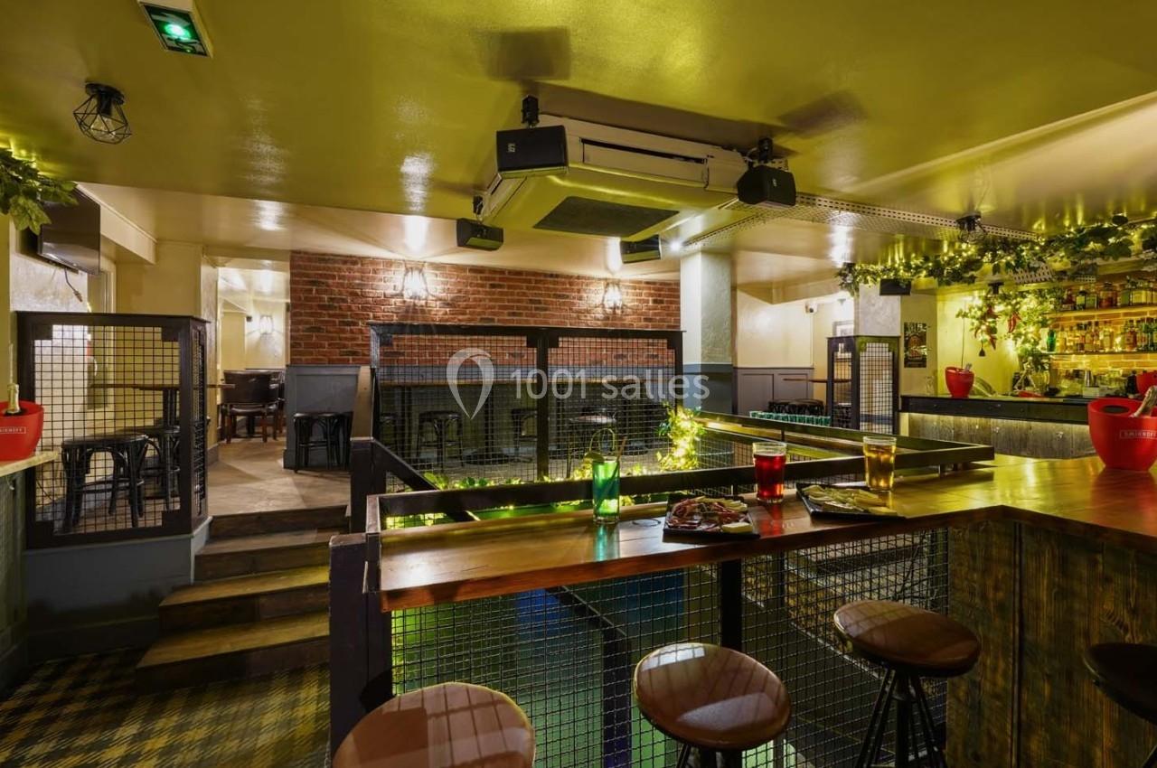 Intérieur d'un bar chaleureux avec comptoir en bois, tabourets, éclairage tamisé et décorations végétales.