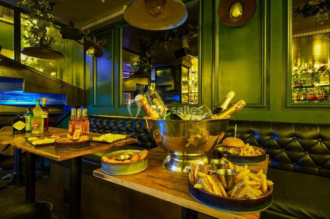 Salle de restaurant avec banquettes vertes, tables en bois garnies de plats variés et seau à champagne au centre.