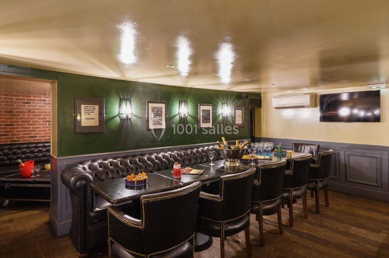Salle à manger avec table en bois, chaises en cuir, murs verts décorés de cadres et éclairage tamisé.