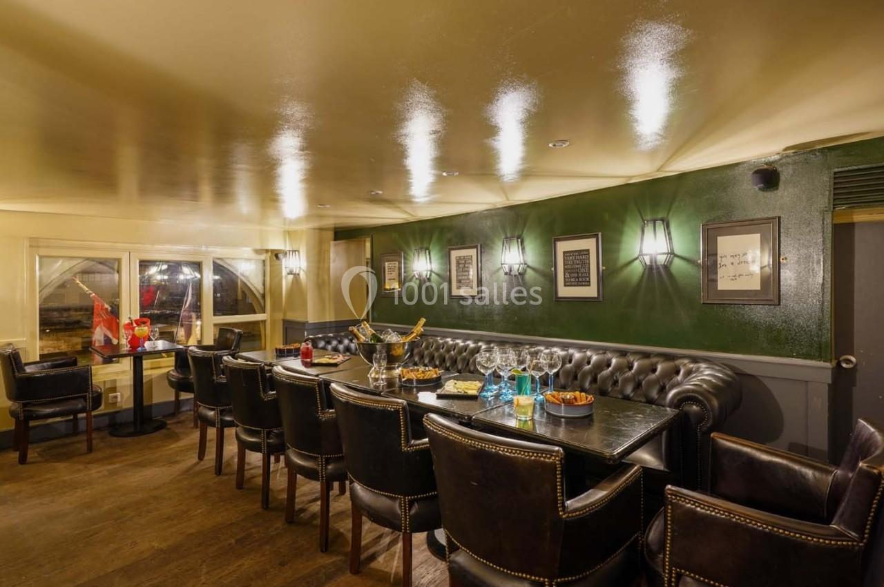 Salle élégante avec canapé en cuir, table dressée avec boissons et snacks, éclairage chaleureux et décor sobre.