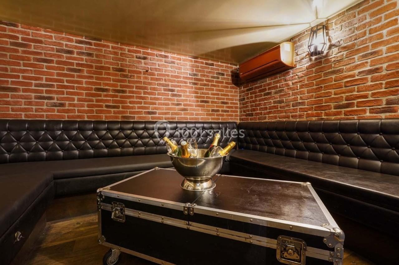 Salle avec murs en briques, banquettes en cuir noir et table basse avec un seau contenant des bouteilles de champagne.