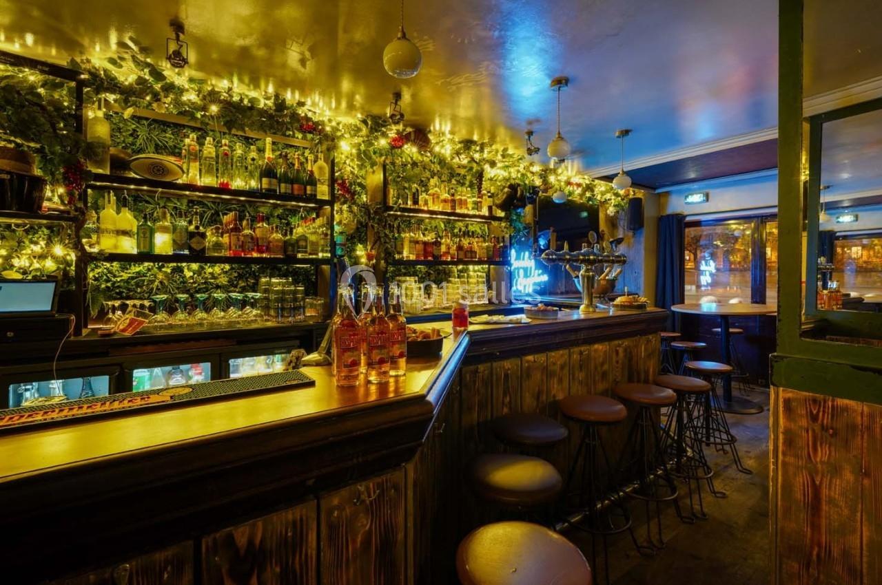 Intérieur d'un bar chaleureux avec comptoir en bois, étagères garnies de bouteilles et éclairage tamisé.