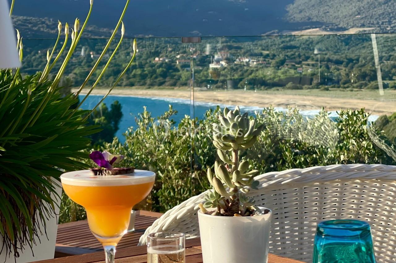 Cocktail sur une table en terrasse avec vue sur un lac, des montagnes et une végétation environnante.