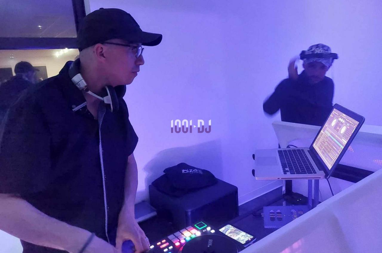 Un DJ mixe sur une table de mixage avec un ordinateur portable, dans une ambiance lumineuse violette.