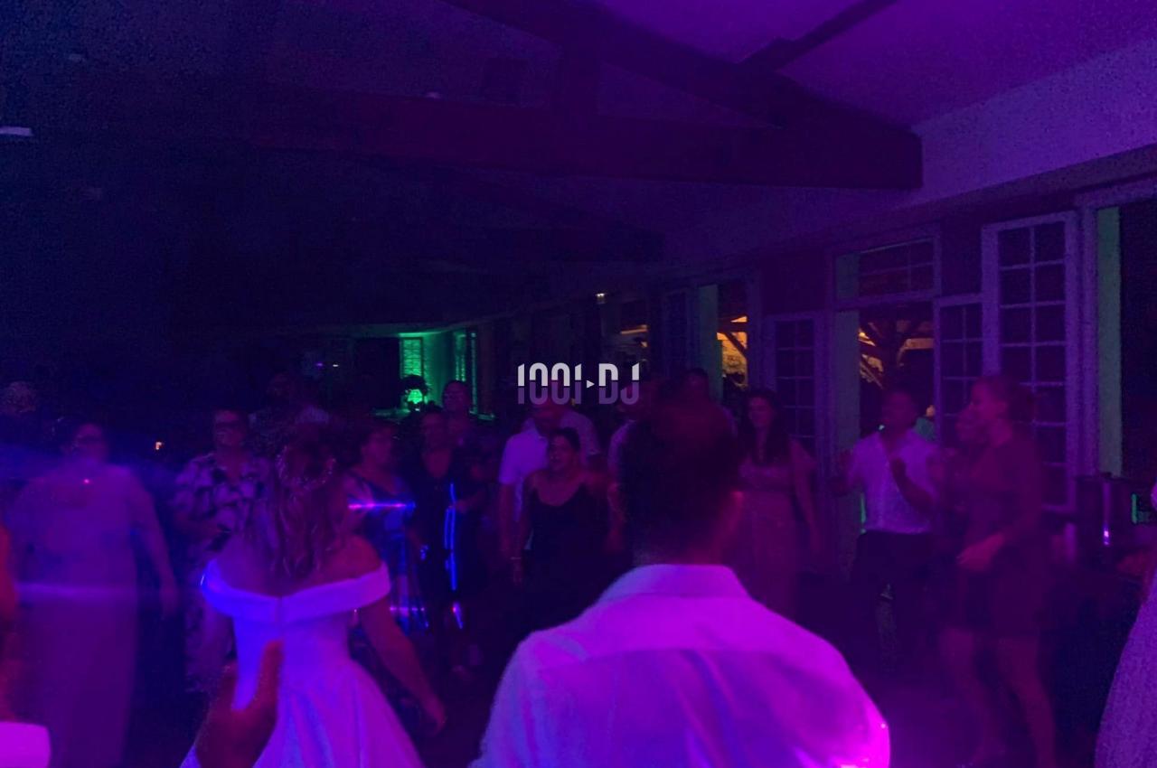 Des personnes dansent dans une salle faiblement éclairée avec des lumières colorées, lors d'une fête ou d'un événement.