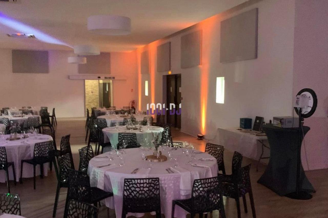 Salle de réception décorée avec des tables rondes dressées, chaises noires et éclairage tamisé.