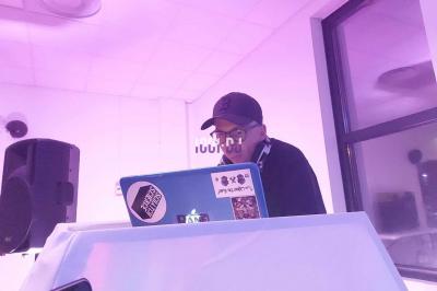 Un DJ mixant de la musique sur une table de mixage dans une salle éclairée par des lumières violettes.