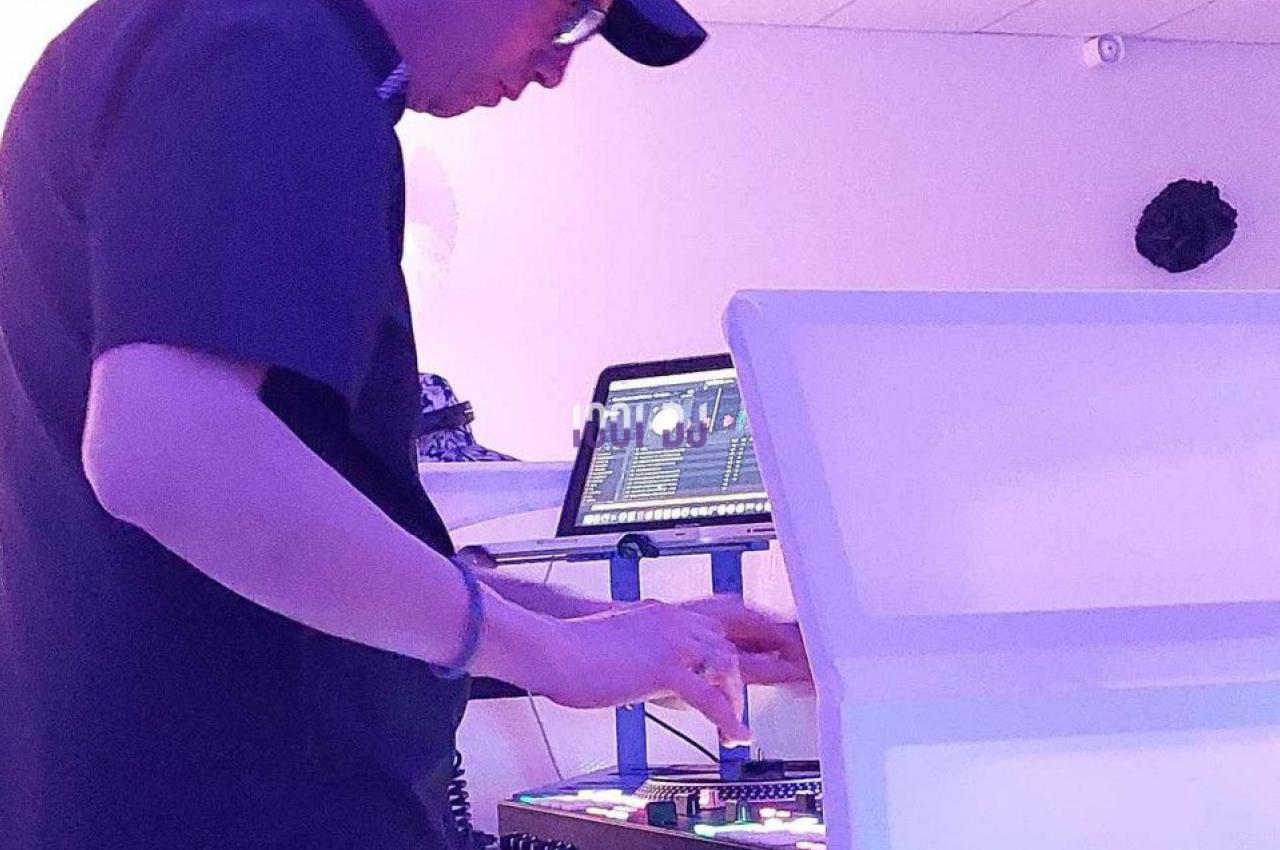 Un DJ mixant de la musique sur une table de mixage dans une salle éclairée par des lumières violettes.