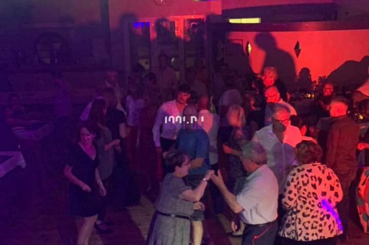 Des personnes dansent dans une salle éclairée par des lumières colorées et une boule disco suspendue au plafond.