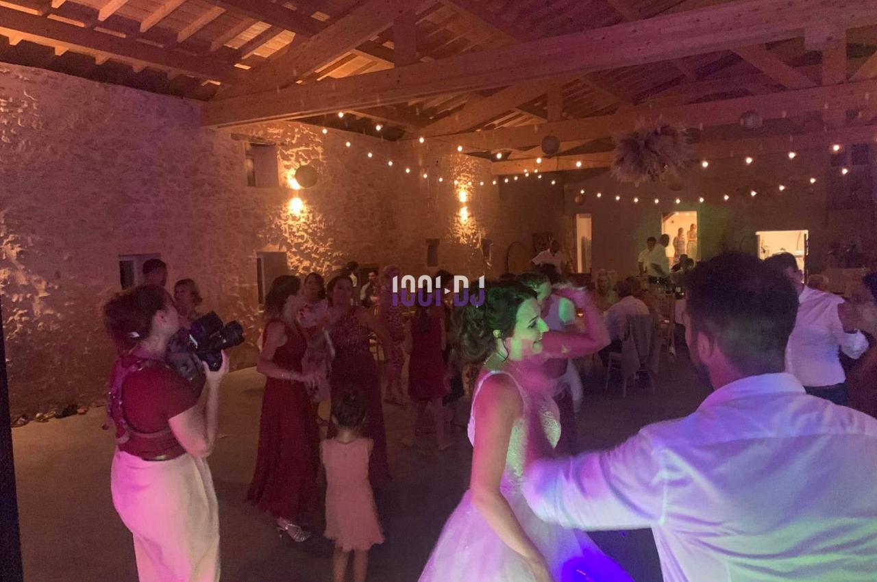 Des invités dansent lors d'une fête dans une salle en pierre éclairée par des guirlandes lumineuses.