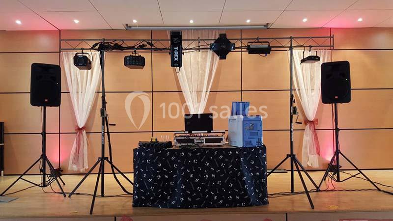 Installation de matériel de sonorisation et d'éclairage sur une scène avec rideaux et éclairage d'ambiance.