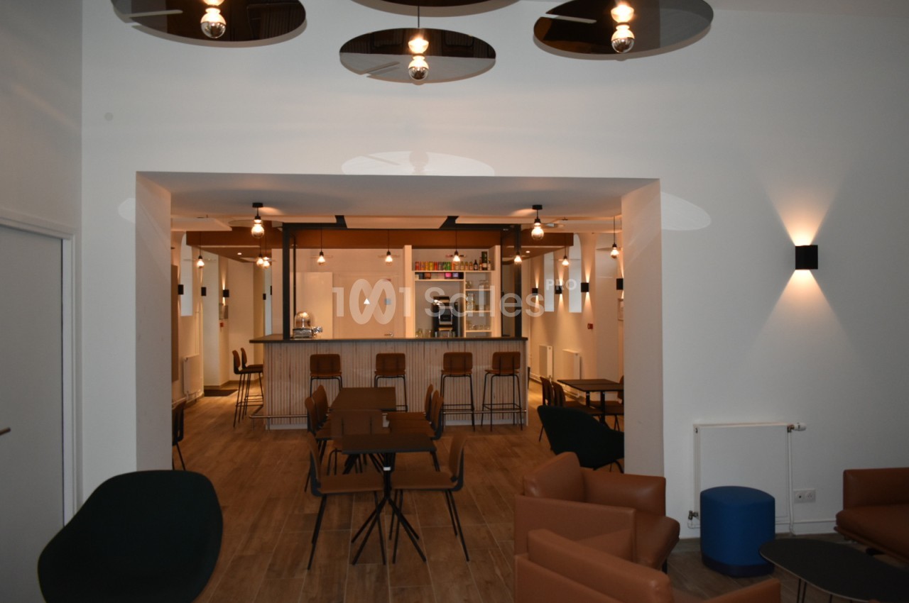 Espace intérieur moderne avec tables, chaises et un comptoir de bar éclairé par des suspensions.