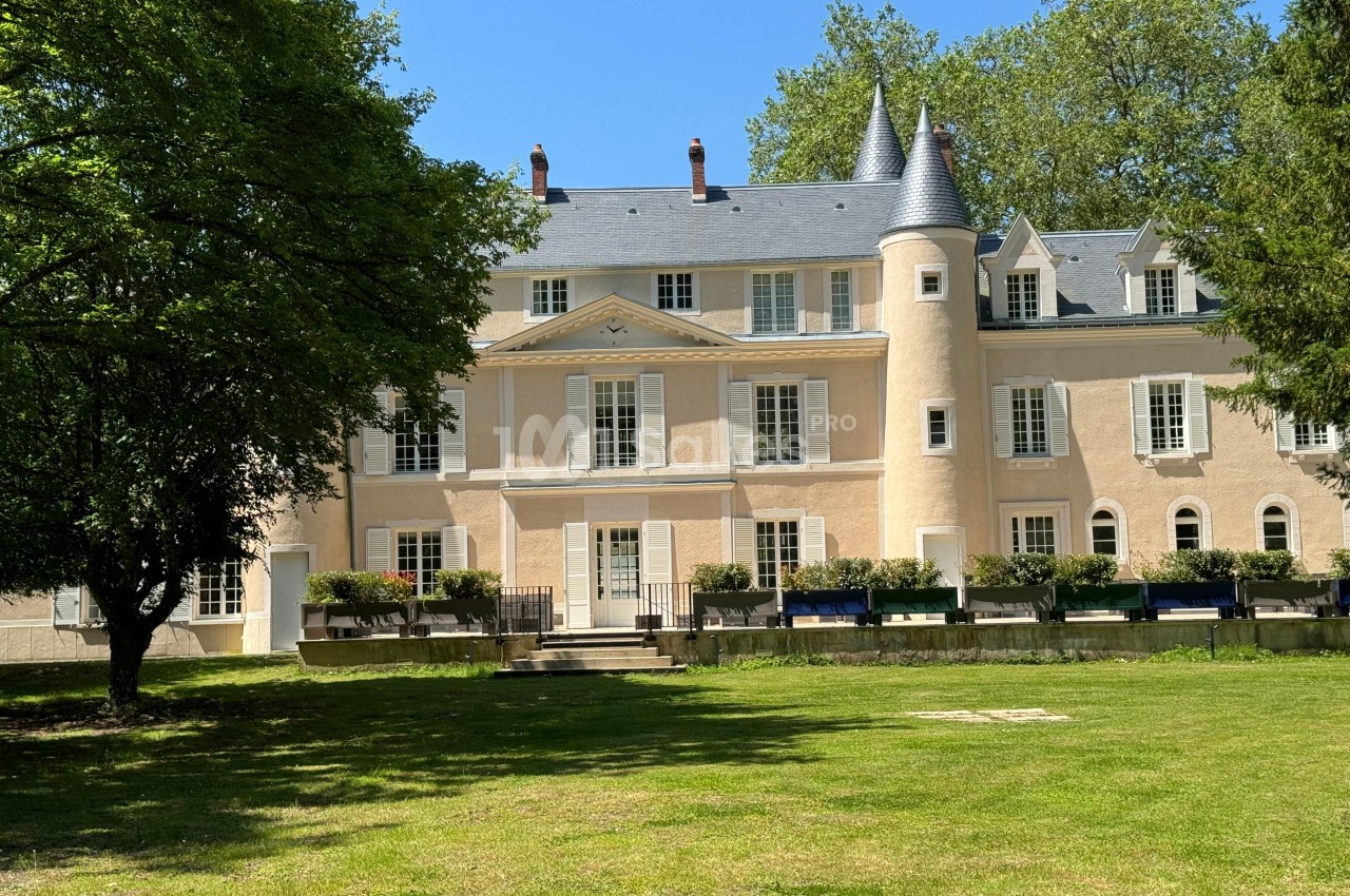 Façade d'un château beige avec tourelles, entouré d'arbres et donnant sur une pelouse verdoyante.