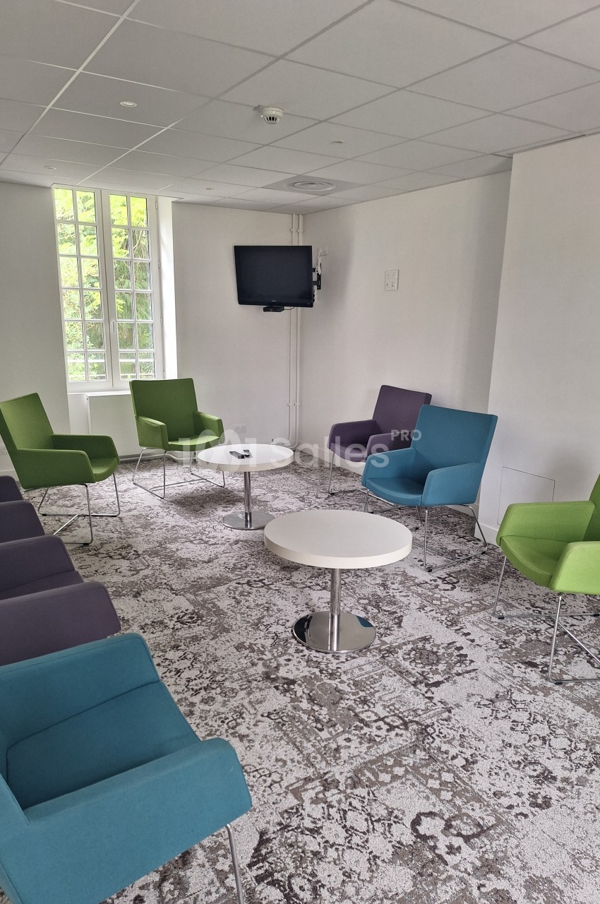 Salle lumineuse avec plusieurs fauteuils colorés disposés en cercle autour de petites tables basses blanches.