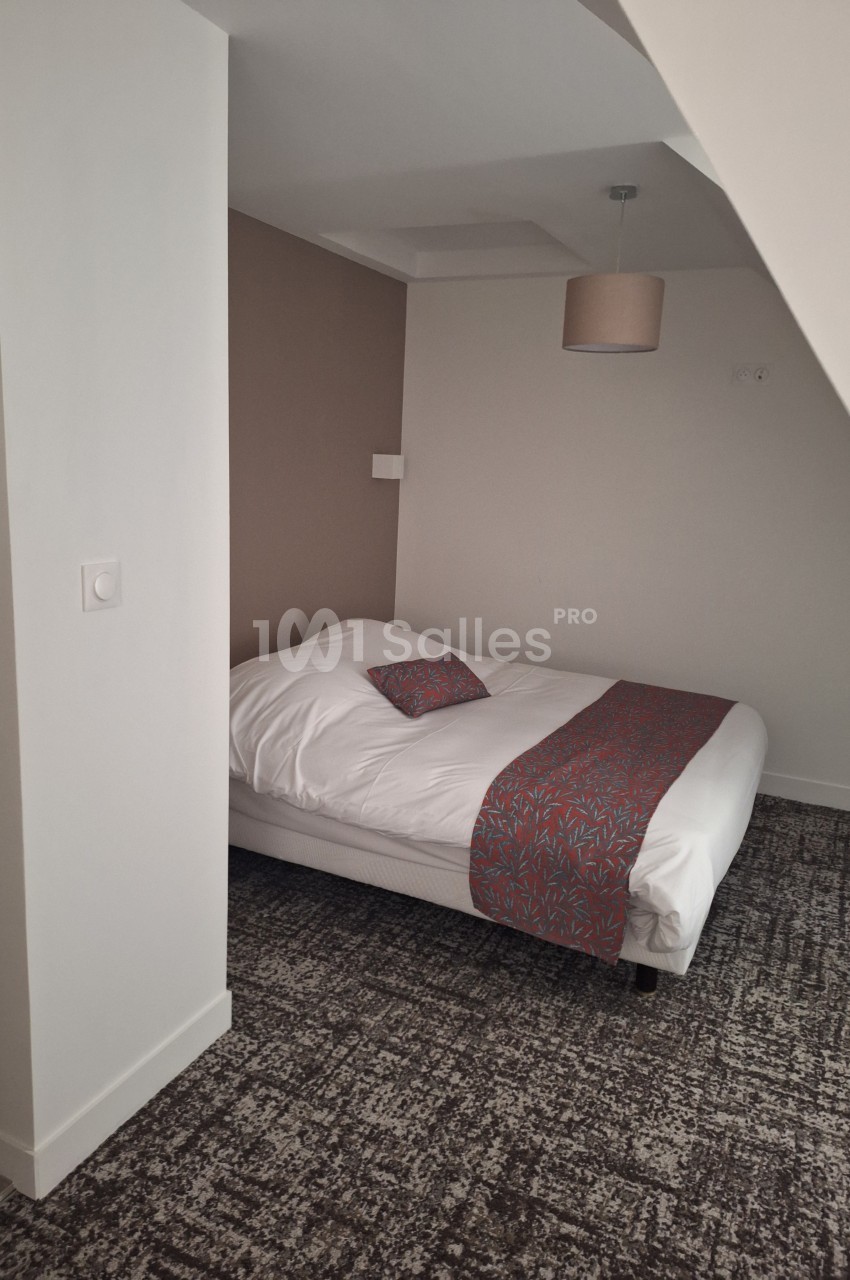 Lit double avec couverture et coussin décoratifs rouges dans une chambre aux tons neutres, éclairée par une suspension.