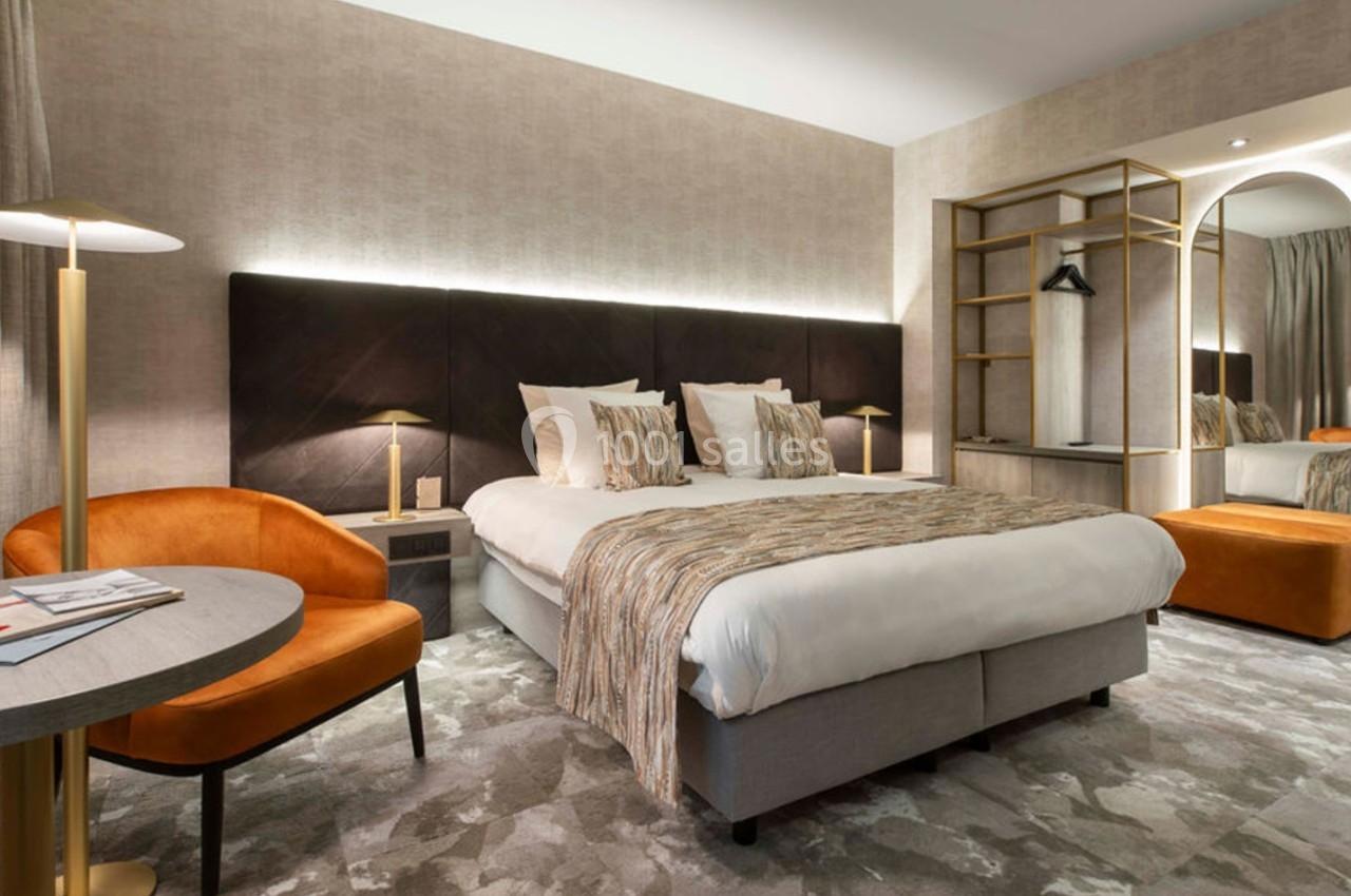 Chambre moderne avec lit double, fauteuil orange, bureau, éclairage doux et miroir près d'une armoire ouverte.