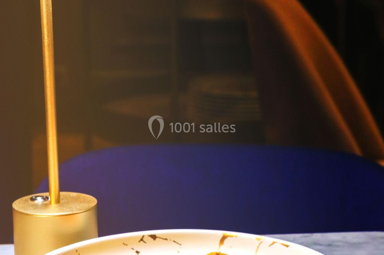 Assiette de raviolis servis sur une table en marbre, éclairée par une lampe, avec des mains ajustant un élément au-dessus.
