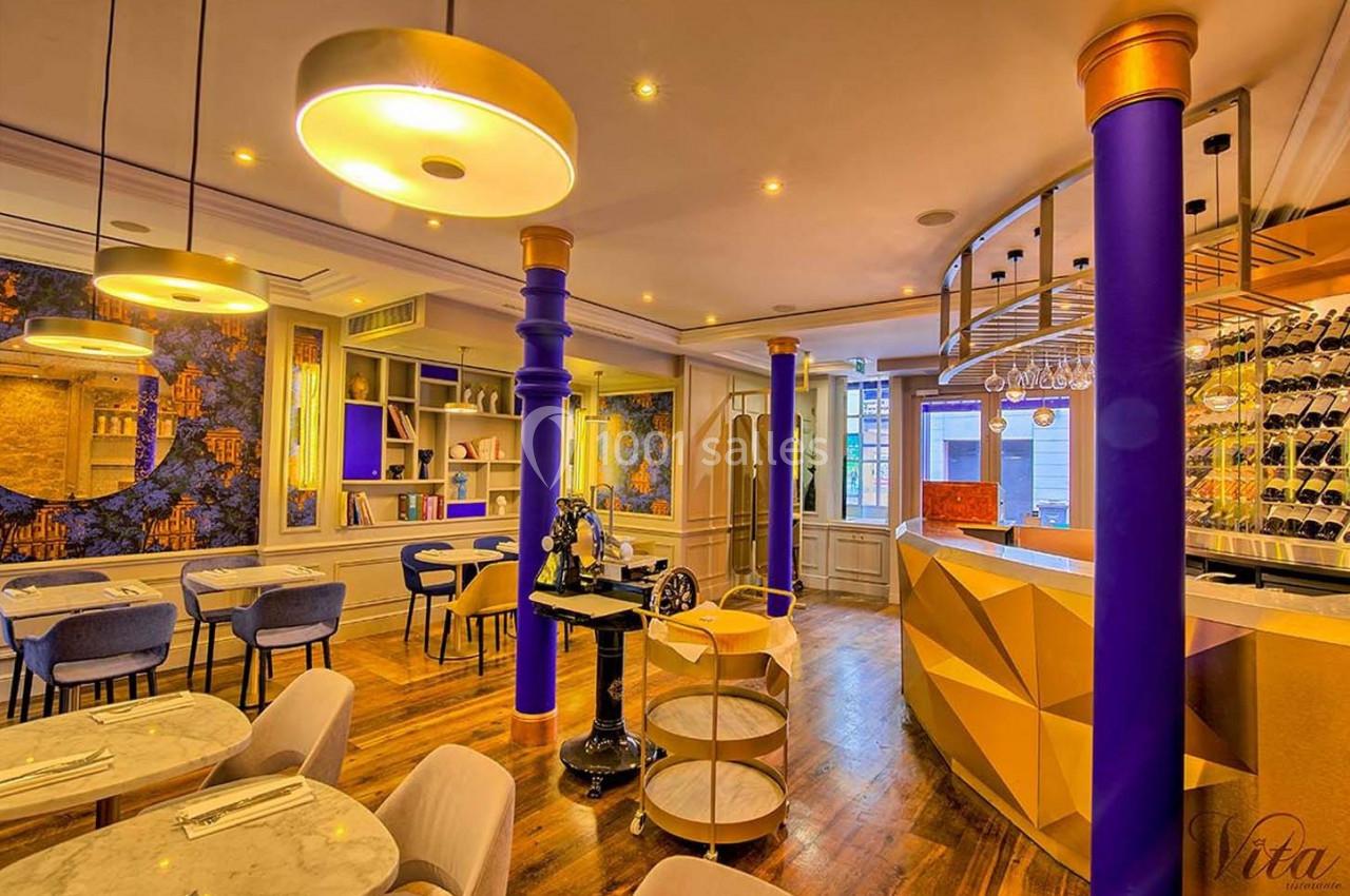 Salle de restaurant lumineuse avec décor coloré, colonnes violettes, tables en marbre et étagères murales.