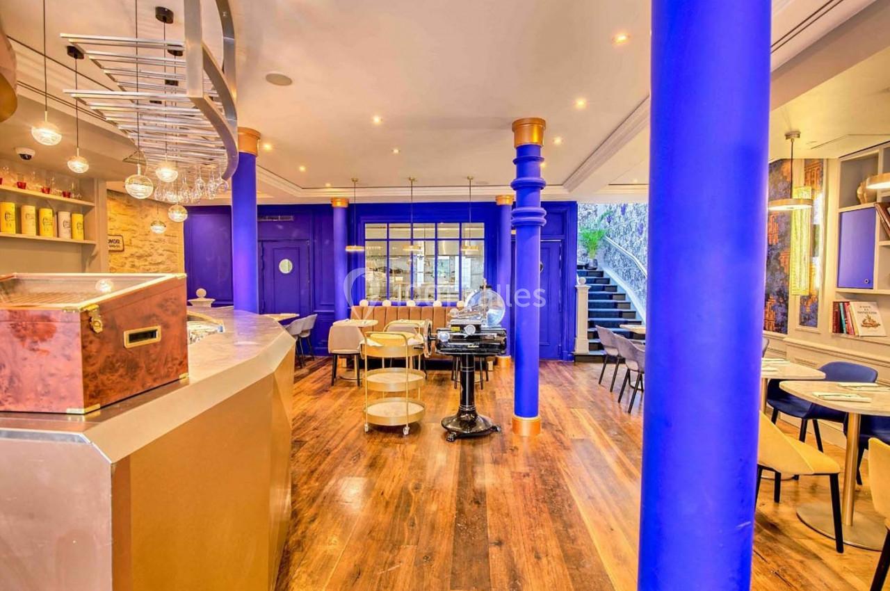 Intérieur d'un café lumineux avec des colonnes bleues, un bar en bois, des tables et des chaises modernes.