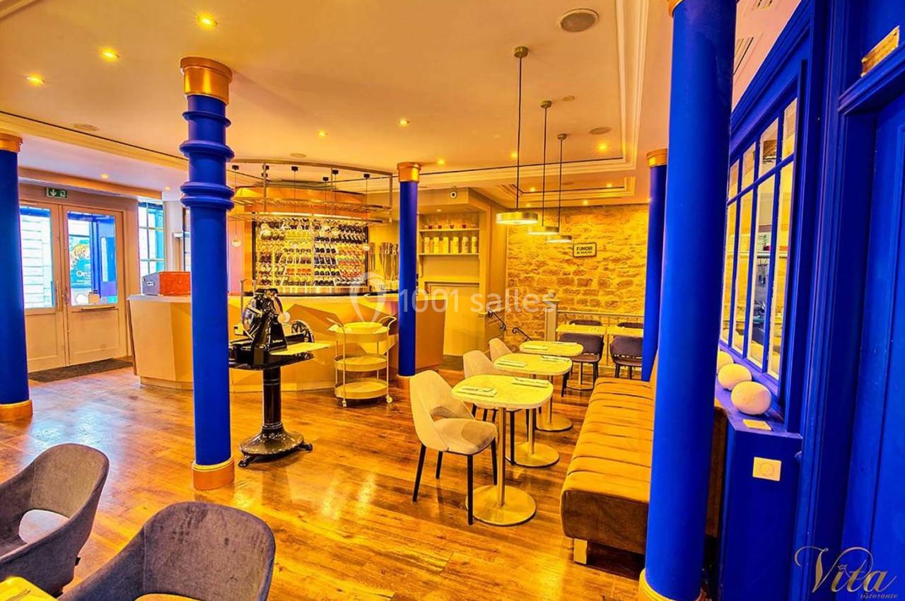 Intérieur d'un restaurant lumineux avec tables, chaises modernes, murs en pierre et bar équipé de bouteilles.