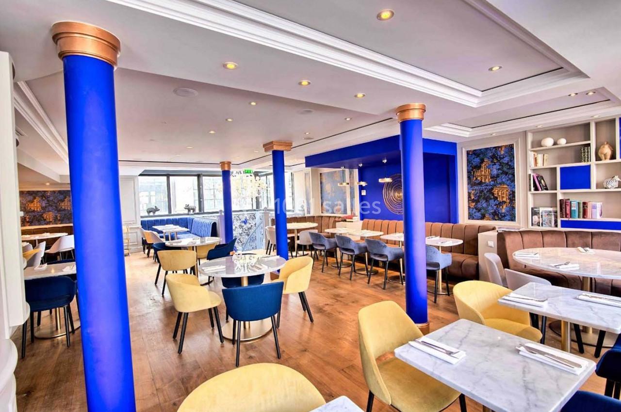 Salle de restaurant lumineuse avec des colonnes bleues, des tables en marbre, des chaises colorées et une décoration moderne.
