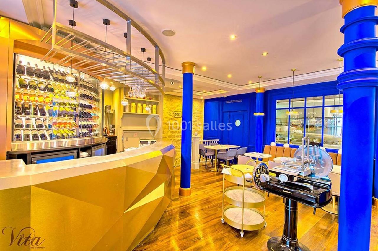 Intérieur d'un restaurant avec comptoir doré, étagères à bouteilles, murs colorés et mobilier moderne.