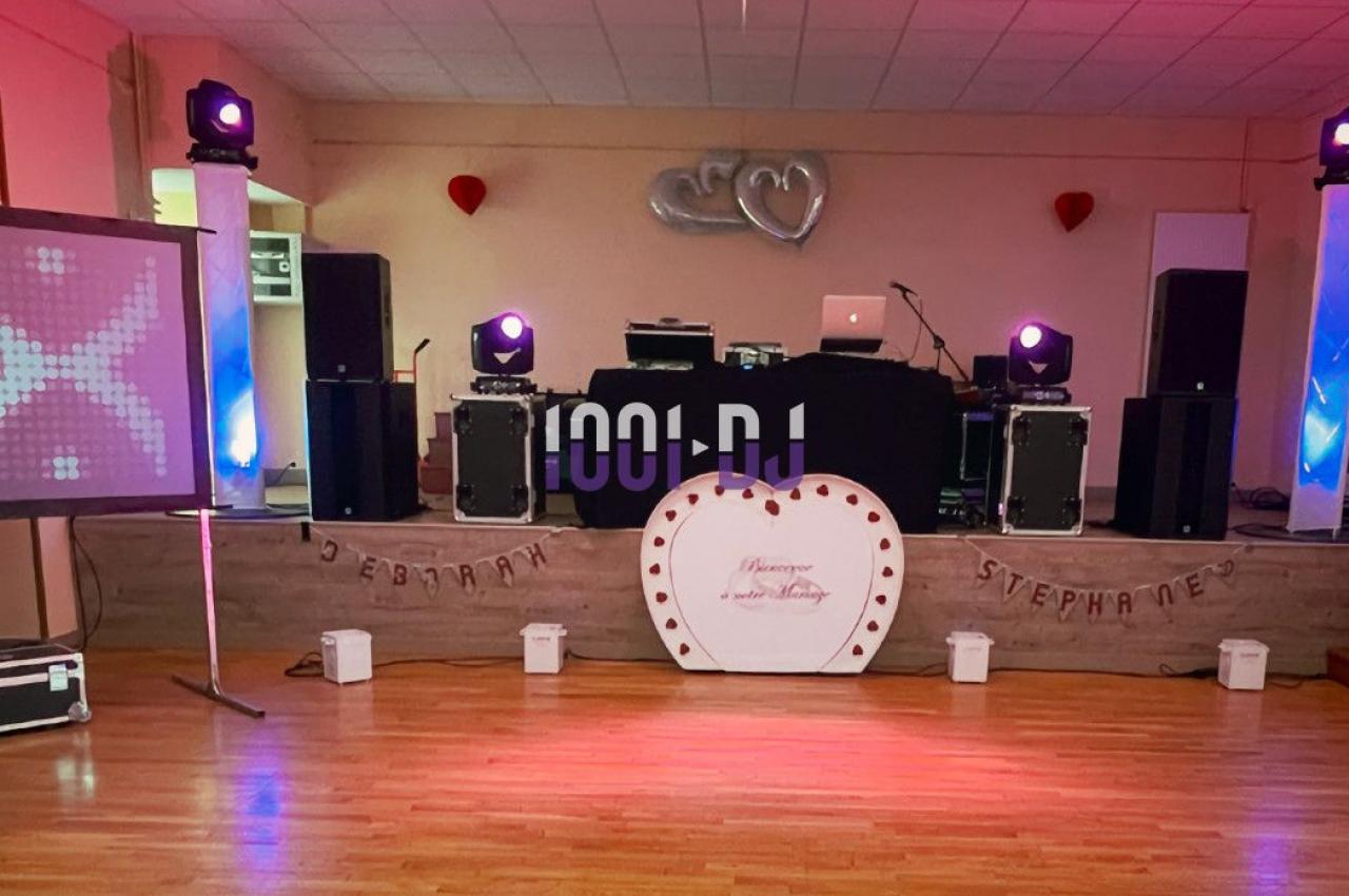 Salle décorée pour un événement avec piste de danse, éclairages colorés, écran, et arche de ballons rouges et argentés.