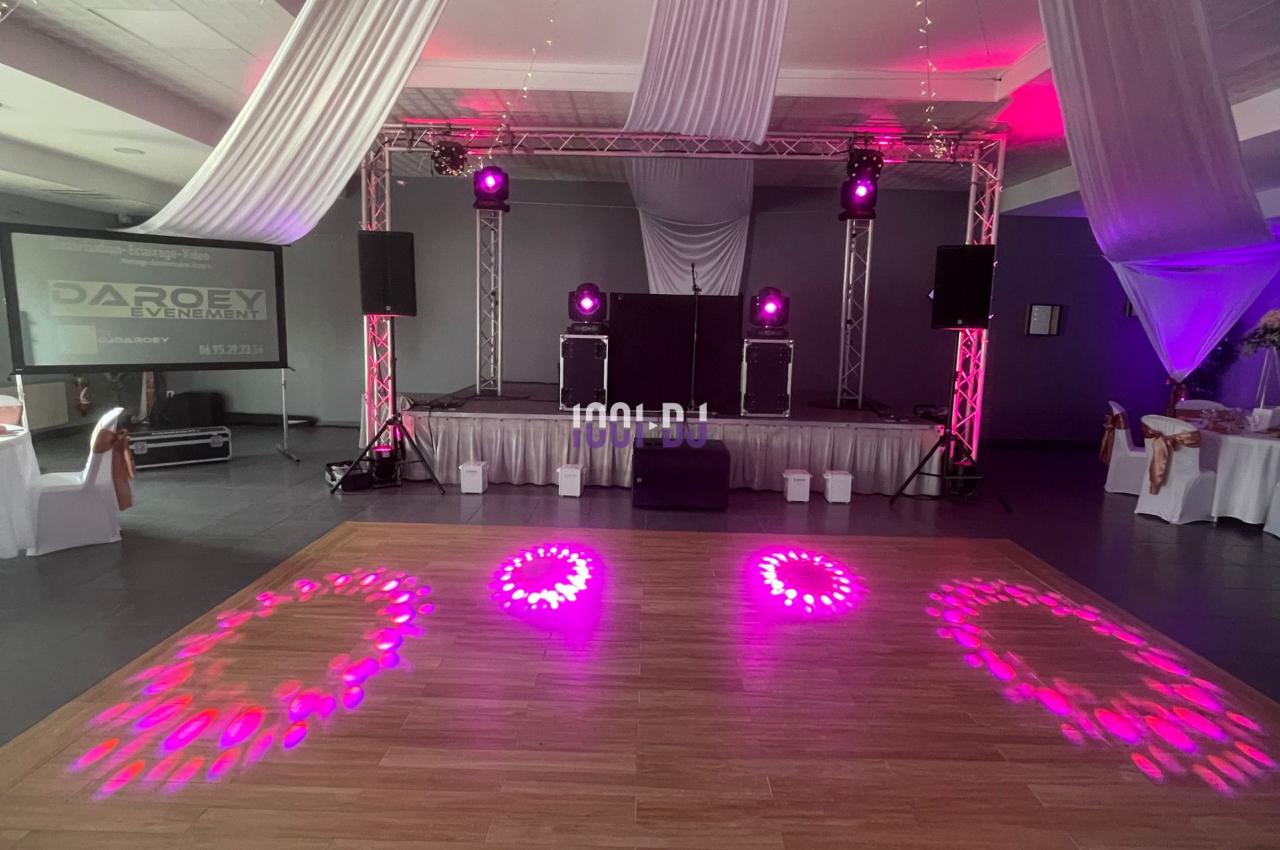 Salle de réception avec piste de danse éclairée par des lumières roses, décorée de voilages et d'un lustre suspendu.