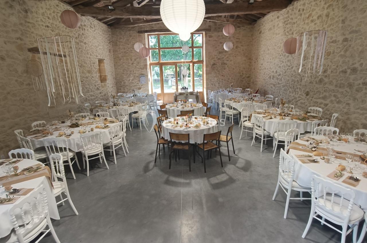 Salle de réception en pierre avec tables rondes dressées pour un événement, décorée de lanternes et suspensions.