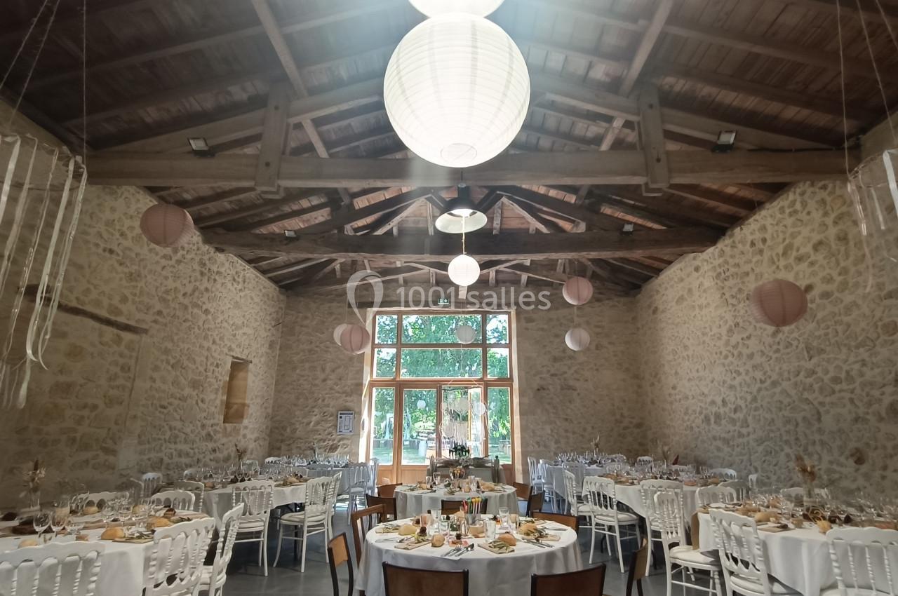 Salle de réception en pierre avec tables décorées pour un événement, éclairée par des lanternes suspendues.