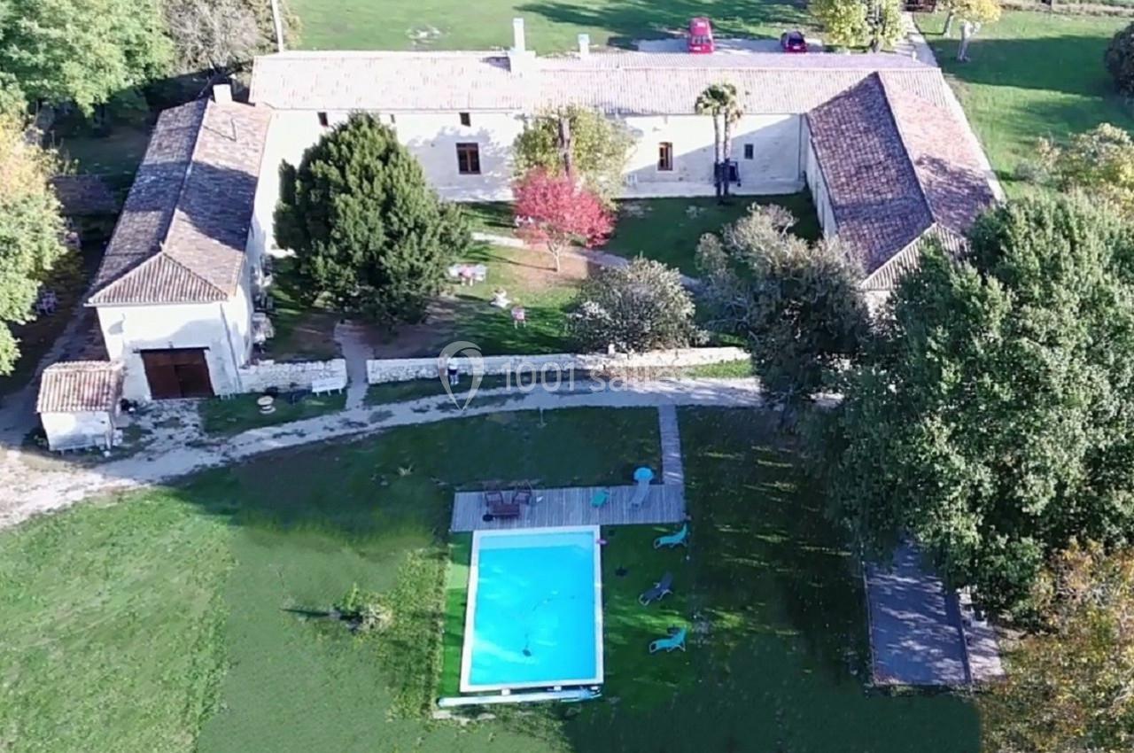 Vue aérienne d'une grande maison en pierre avec une cour, un jardin arboré et une piscine rectangulaire.