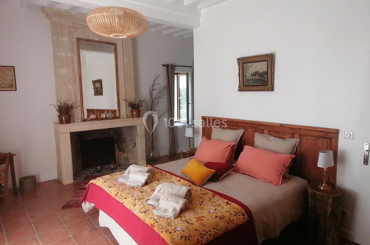 Chambre lumineuse avec lit double, cheminée, bureau en bois et décoration chaleureuse dans un style rustique.