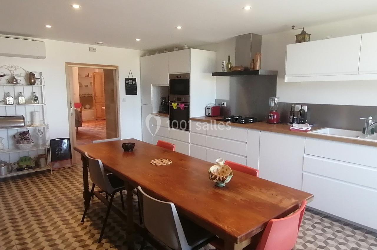 Cuisine moderne avec meubles blancs, table en bois, sol à motifs géométriques et étagères décoratives.