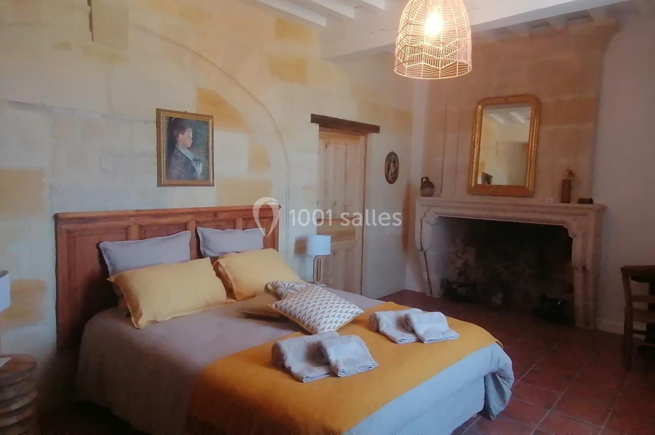 Chambre chaleureuse avec lit double, murs en pierre, cheminée ancienne, miroir doré et éclairage suspendu.