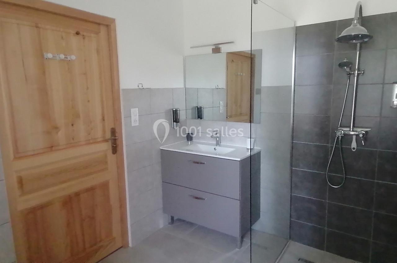 Salle de bain avec douche à l'italienne, meuble lavabo gris, miroir et porte en bois clair.