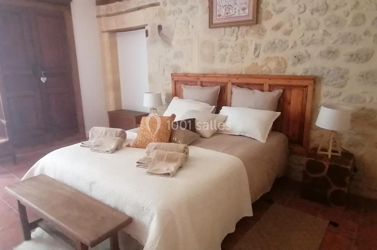 Chambre avec lit double, murs en pierre, mobilier en bois, lampes de chevet et décoration rustique.