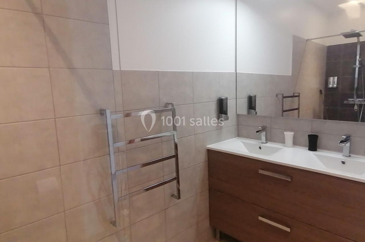 Salle de bain moderne avec carrelage beige, meuble double vasque en bois et miroir, sèche-serviettes mural.