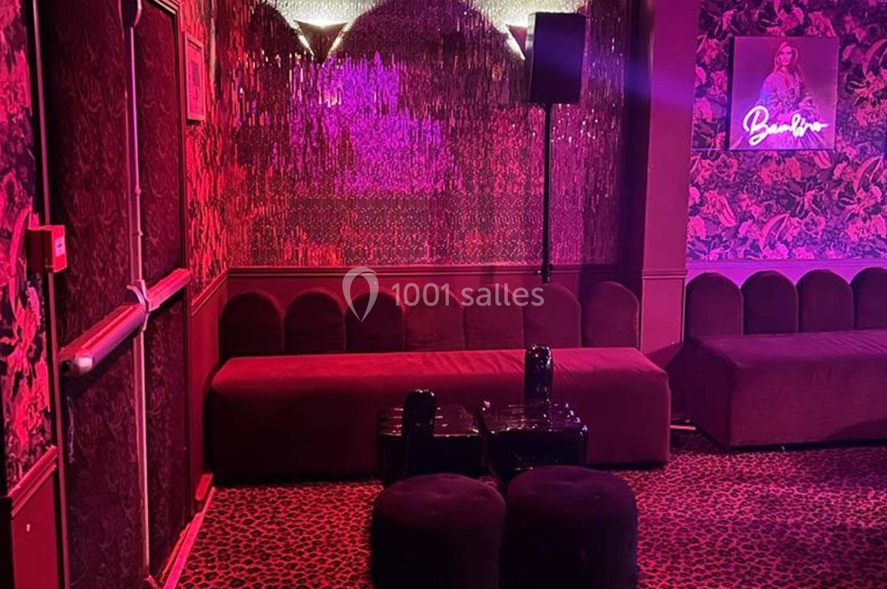 Salle décorée avec des murs rouges texturés, banquettes, tabourets noirs et éclairage tamisé rose.
