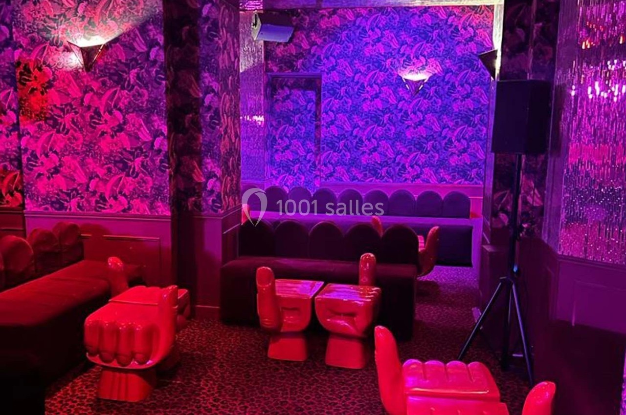 Salle aux murs décorés de motifs floraux violets, éclairée par une lumière rose, avec des sièges originaux en forme de mains.