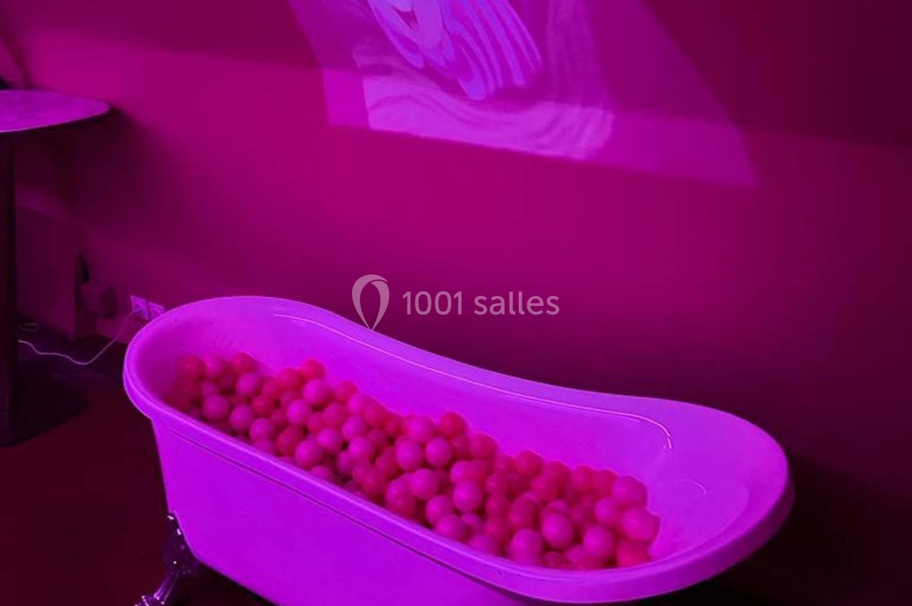 Baignoire blanche remplie de balles roses dans une pièce éclairée par une lumière rose.