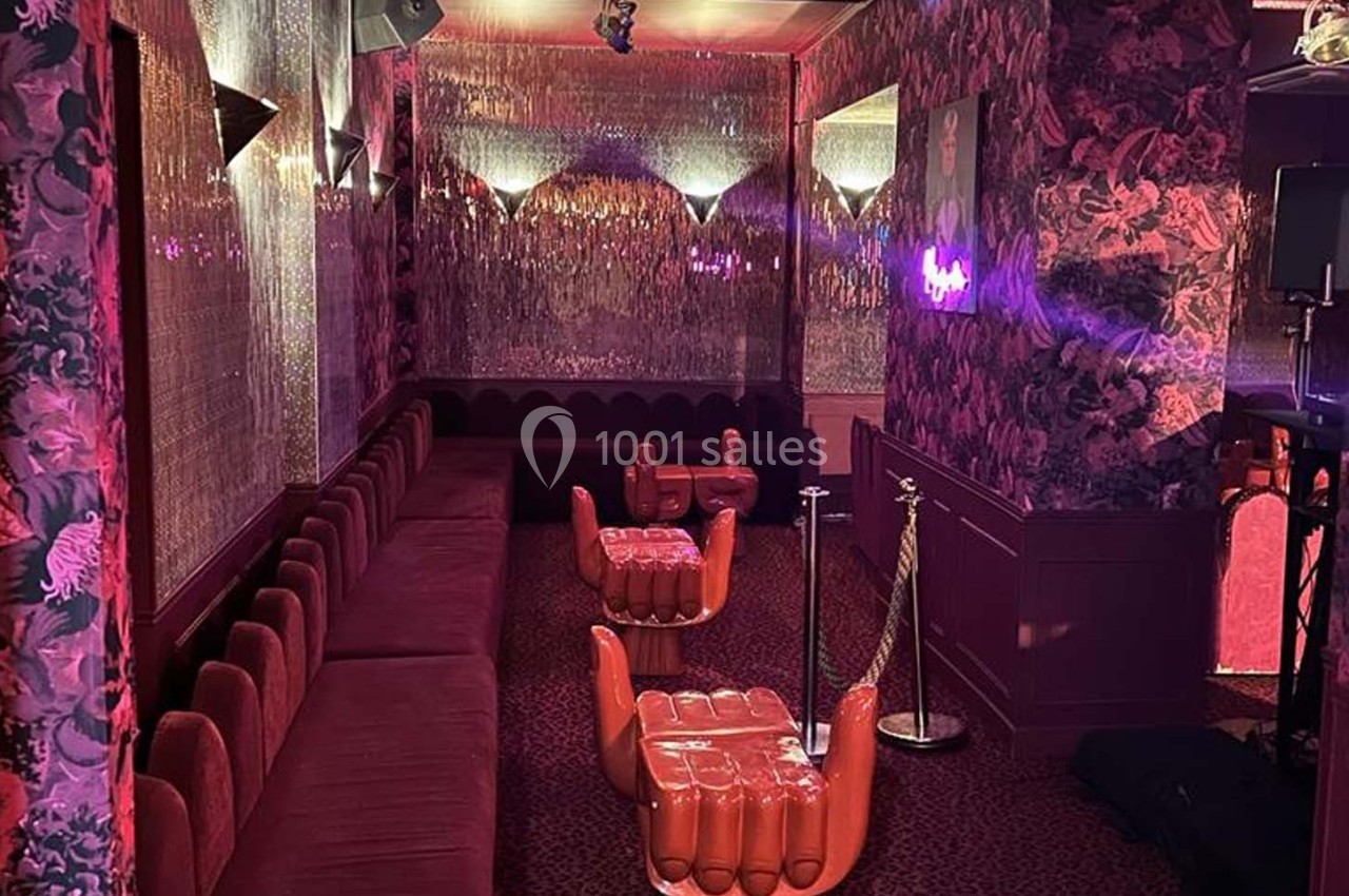Salle décorée avec des banquettes rouges, murs fleuris et sièges en forme de mains sous un éclairage tamisé.